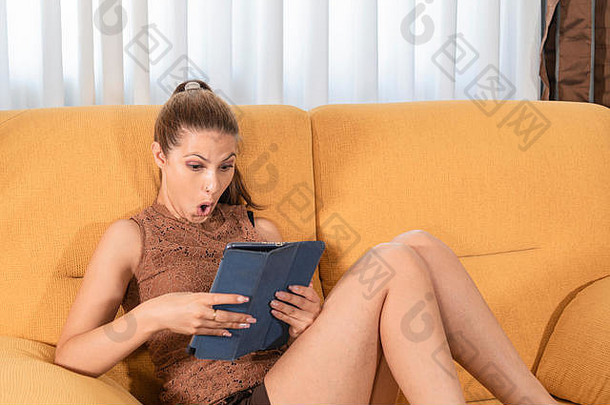 有吸引力的夫人坐着沙发表达惊喜读取平板电脑色彩斑斓的肖像