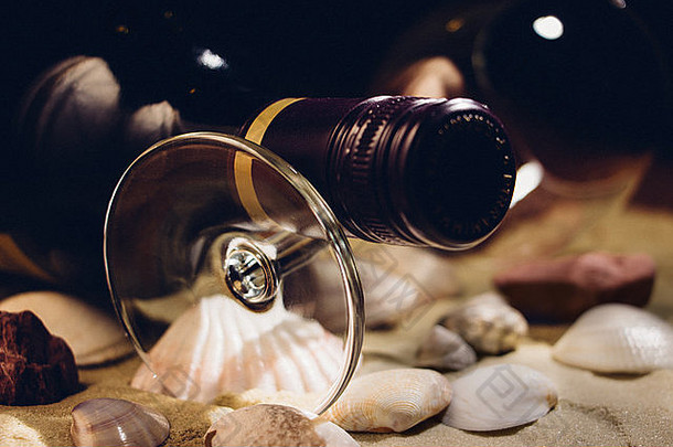 一瓶未开封的红<strong>酒</strong>，放在沙子和贝壳上的玻璃杯上。胶卷外观，纹理效果。