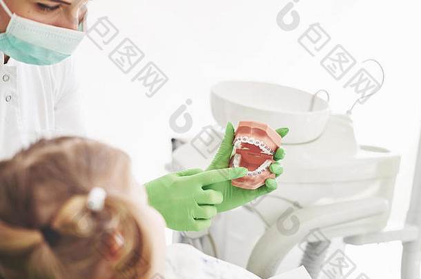 坐在牙医椅上的小女孩，正在接受儿科牙医关于正确刷牙的教育。早期预防及口腔卫生概念