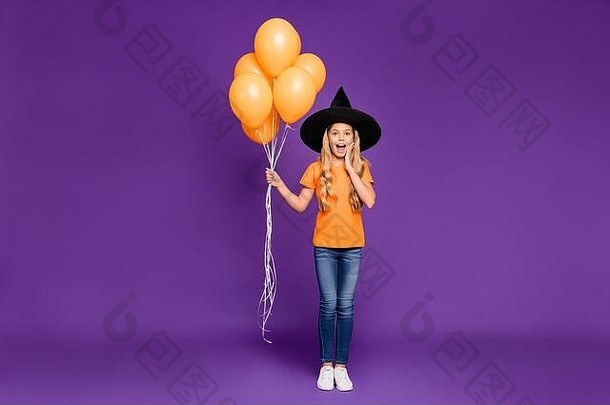 兴奋的小女士万圣节派对的全尺寸照片拿着气球来到儿童主题派对穿橙色t恤女巫帽隔离紫色