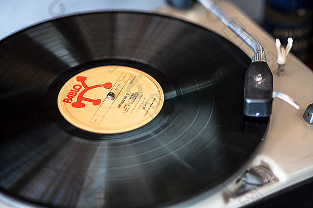 一张经典爵士乐巴勃罗唱片集的特写照片，在转盘上播放，音色为手臂和头部外壳。乙烯基本身有轻微的运动模糊。