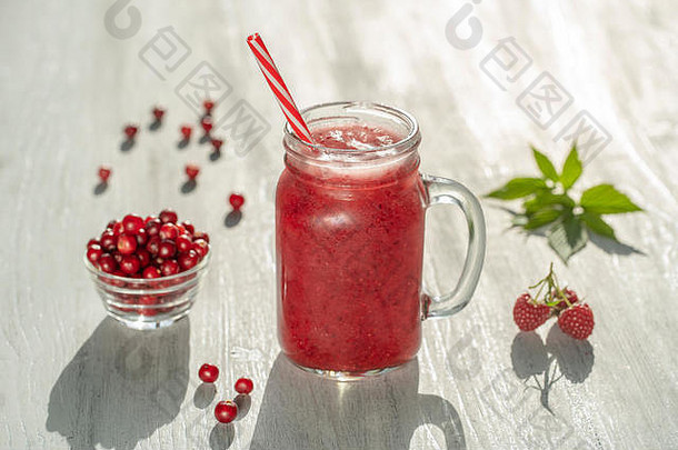 白色桌子上的玻璃杯子中的新鲜有机红色思慕雪，特写。清爽夏日水果饮料。健康饮食的概念。蔓越莓和覆盆子
