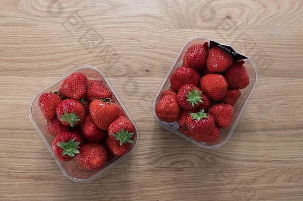 木桌上放着两个草莓塑料网。鲜美的红色水果。不环保。回收必须使用塑料容器