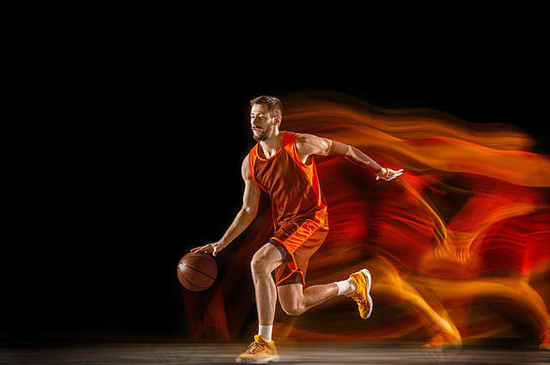 彗星。红队的年轻白人篮球运动员，在黑暗的工作室背景下，在混合光线下进行动作。运动、运动、活力和健康生活方式的概念。