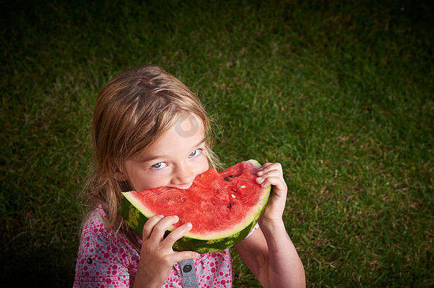 可爱的金发小女孩夏天在草地上吃西瓜