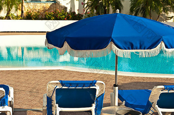 蓝色雨伞和椅子沿着游泳池排列。