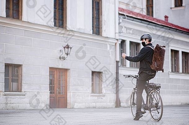 送货员骑着自行车带着面罩和智能手机在城里送货。