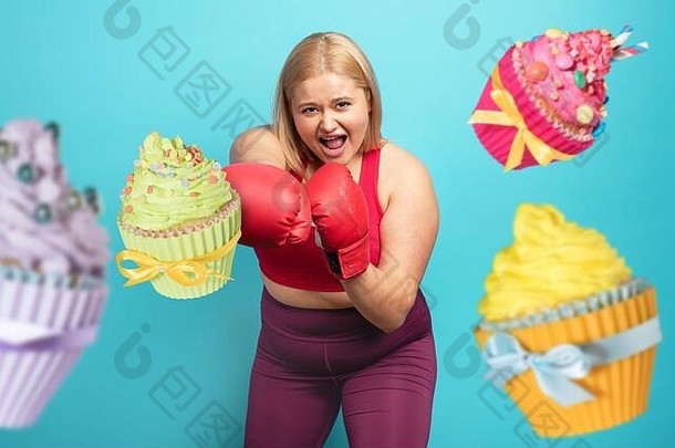 健身套间里的胖女孩<strong>打拳击</strong>和对抗纸杯蛋糕。青色背景