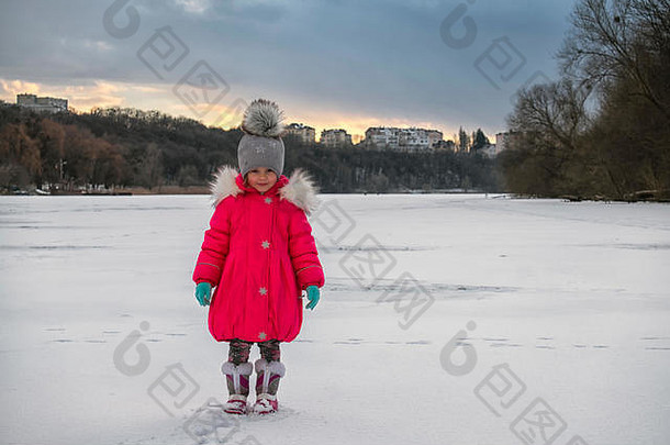 穿着红色羽绒服的小女孩站在一条冰冻的河流中间