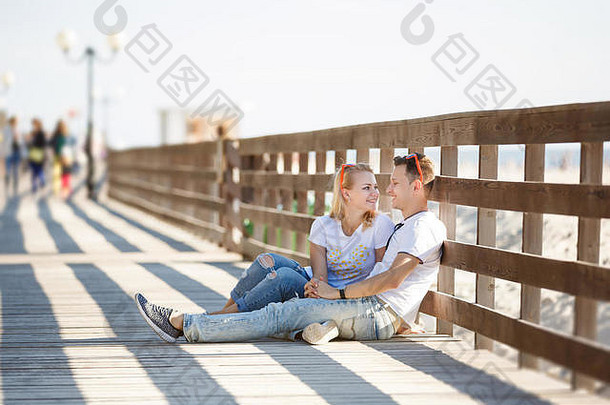 夏天，一对快乐的夫妇坐在海滩上的木栅栏旁