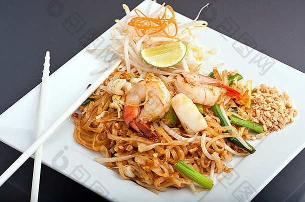 海鲜将泰国炒饭面条放在一个方形的白色盘子上，用筷子和磨碎的胡萝卜装饰。