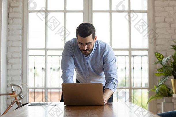 年轻成功的男经理靠在桌子上写电子邮件。