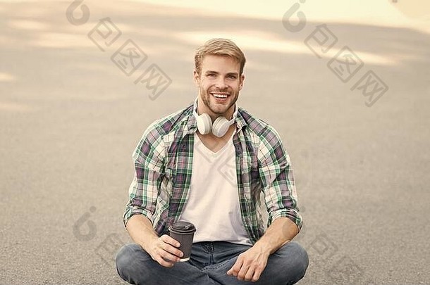 要高兴。男式格子衬衫。学生放松和充电。咖啡带走。那个家伙在户外喝咖啡。那个人坐在地上。戴着耳机的无忧无虑的学生。在线教育。听音乐。电子书概念。