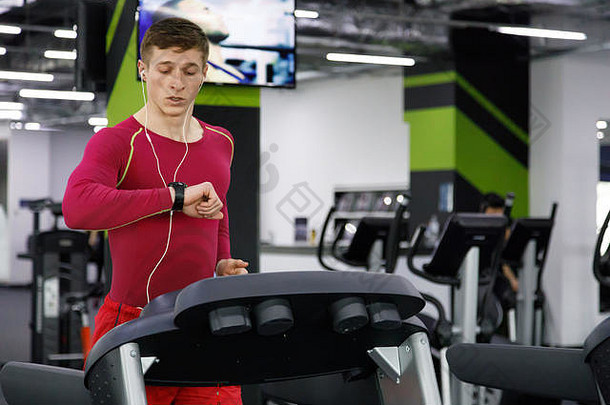 完整的长度肖像肌肉发达的运动员听音乐耳机<strong>手表</strong>跑步机现代健身房