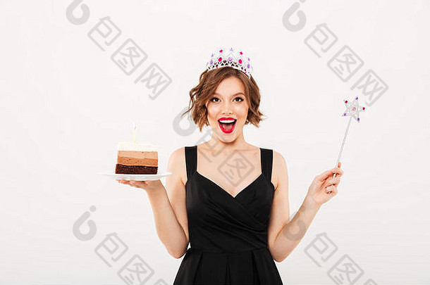 一个快乐女孩的肖像，穿着戴着<strong>皇冠</strong>的盘子，拿着一块生日<strong>蛋糕</strong>，在白色背景下庆祝