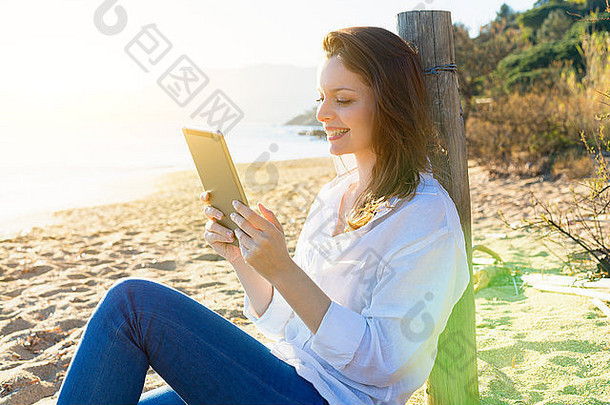 在海滩上使用数字平板电脑的女人