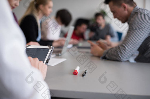 商人用平板电脑双手的特写镜头，办公室会议室里的人群模糊在背景中