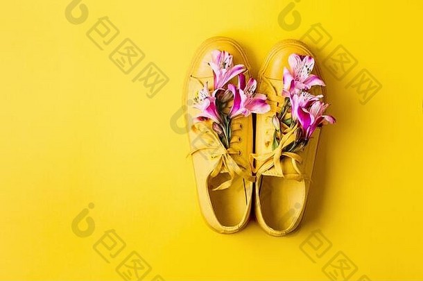 一双黄色运动鞋和黄色背景上的花蕾。春夏时尚概念，空间。