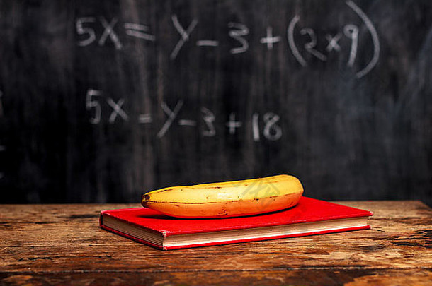 书和香蕉放在黑板前的桌子上，上面有<strong>数学题</strong>
