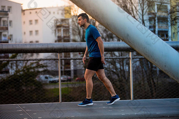 男子跑步者在城市公园里跑过桥进行健身训练。夏天，一名男子在城市公园的一座桥上跑步。