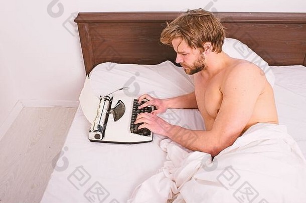 这位男作家躺在床上，白色的被褥正在写新书。早晨灵感的概念。盖伊用打字机创建新章节。作者过去习惯于使用老式机器而不是数码设备。