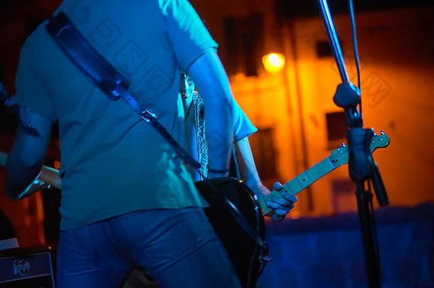 一位摇滚音乐家在烟雾和柔和灯光的音乐会上现场演奏贝司的细节。带有滤光镜头的艺术照片。