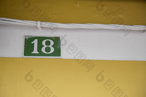 在西班牙，黄色墙壁上的白线上镶嵌着绿色搪瓷板上的白色18。