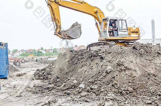 黄色挖掘机正在施工现场向自卸卡车填土，<strong>项目</strong>正在进行中。