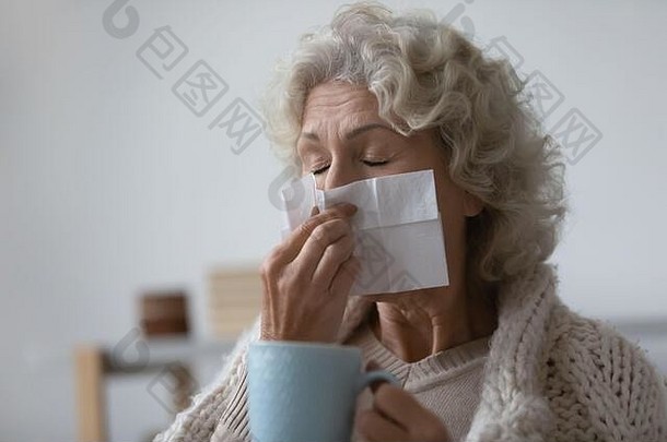 不健康的老妇人用纸巾擦流鼻涕。