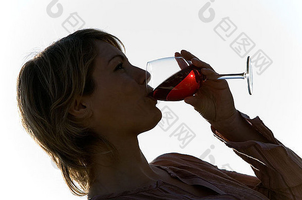 一个年轻的金发女人的侧影，喝着杯里的红酒，专注于女人