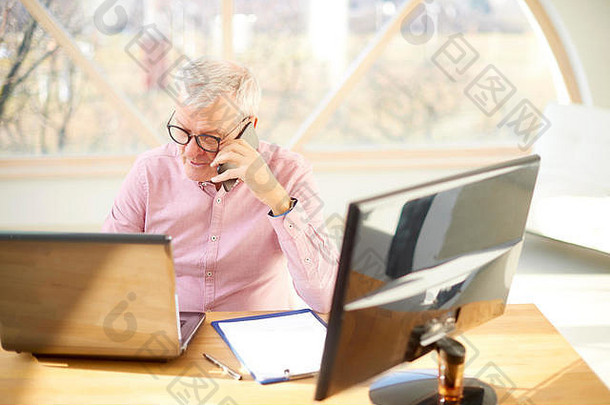 高角拍摄上了<strong>年</strong>纪的商人坐着前面移动PC会说话的移动电话工作硬