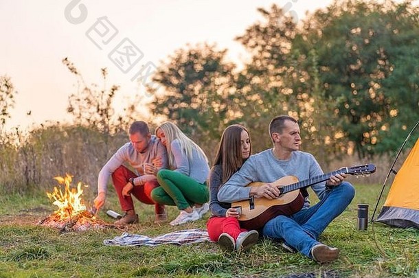 一群带着吉他的快乐朋友，在篝火旁和旅游帐篷旁享受户外的乐趣。露营快乐家庭。