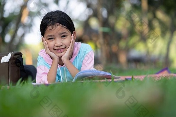 阳光普照的花园里，一个小女孩正在草地上的树下看书。