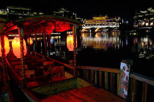 凤凰古城凤凰虹桥下，一艘停靠在码头上的旅游船坐在那里等待游客登上沱江，在凤凰虹桥下漂浮