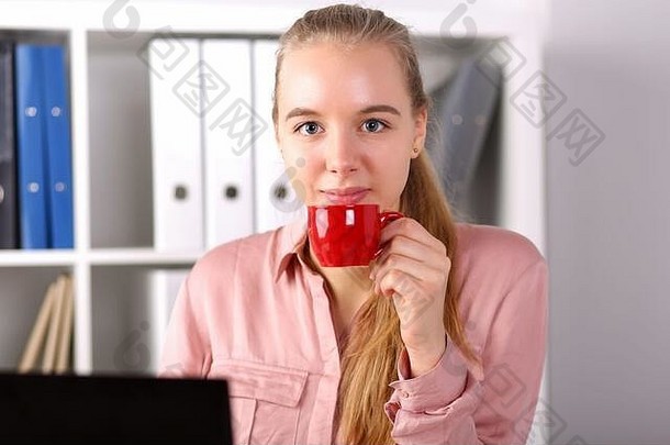 女孩坐在办公室电脑前喝咖啡