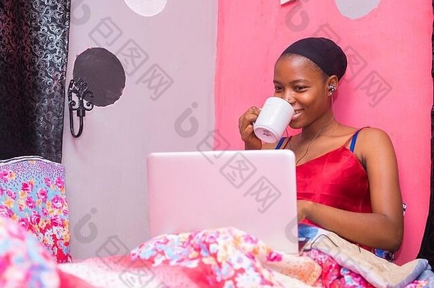 一位漂亮的非洲女士独自一人在卧室里，用笔记本电脑看电影