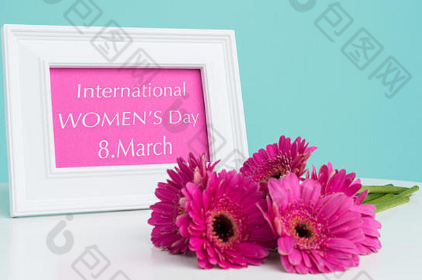 “快乐妇女节”粉彩糖果蓝色背景，深粉色非洲菊，白色相框，印有“快乐妇女节”字样。