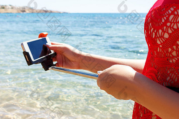 穿着红色泳衣的女孩在海里调整<strong>自拍杆</strong>上的相机。
