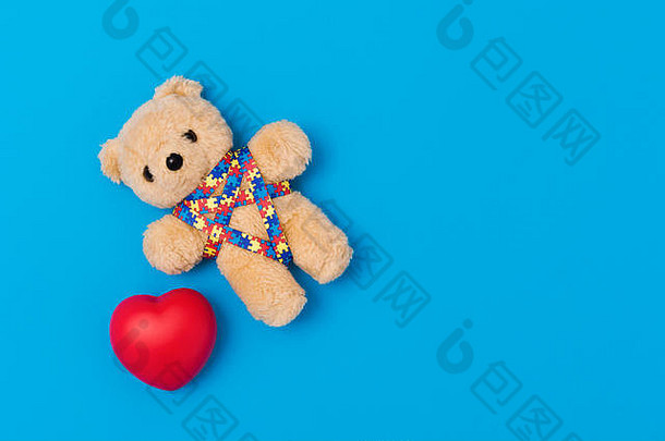 世界孤独症意识日，心理保健概念。红色心形和缎带拼图图案的泰迪熊。在蓝色背景上