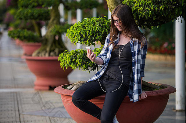 坐在城市公园里使用<strong>智</strong>能手机和发短信的少女
