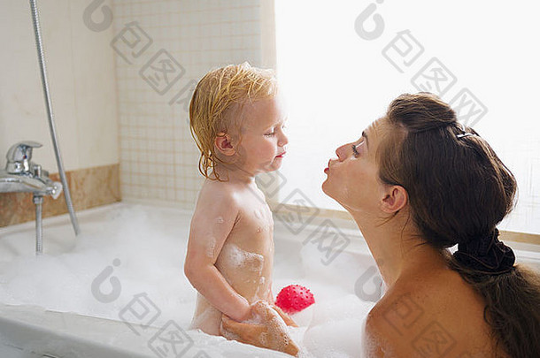 婴儿在充满泡沫的浴缸里洗澡时亲吻母亲