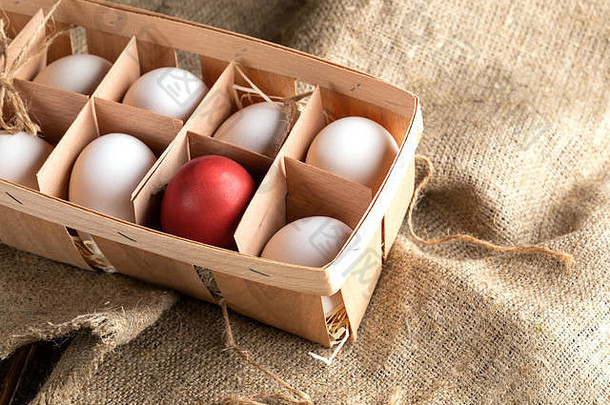 打开环保木箱，在粗麻布上放上白蛋和一个红色复活节蛋。包装箱由薄木皮条制成。
