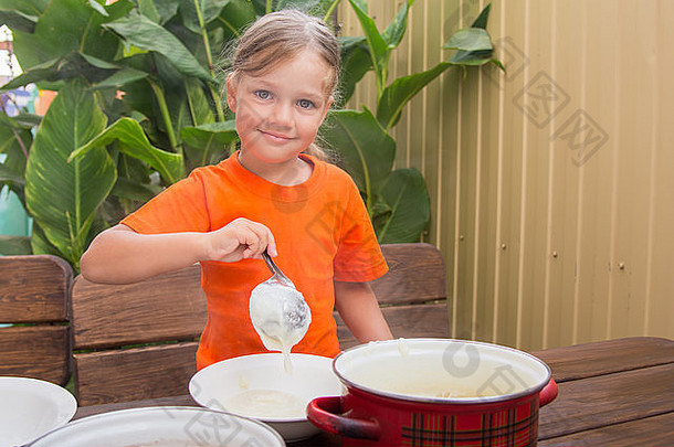 吃早餐的四岁女孩把勺子放进一碗粗面粉里