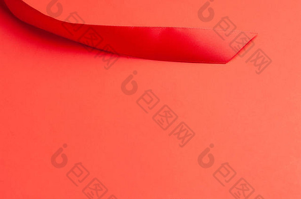 一条中等宽度闪亮的红色缎带的漩涡状尖端，镶嵌在缓慢渐变的纯红色纸背景上。