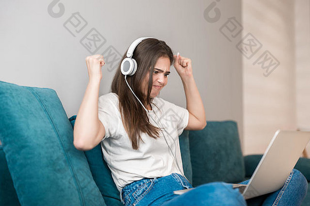 年轻的美丽的女人耳机听音乐移动PC玩视频游戏沙发生活房间赢得了追求
