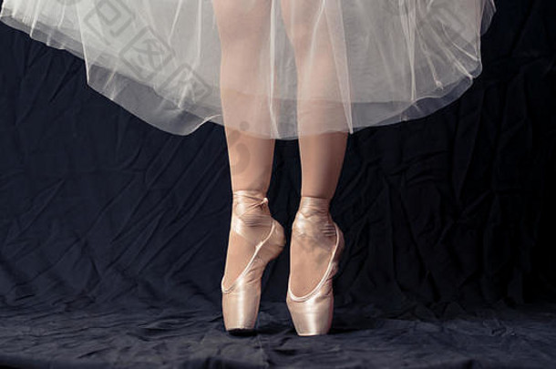 在黑色背景上穿着白色尖头的芭蕾舞演员跳舞腿的特写镜头。芭蕾舞演员与实践概念背景