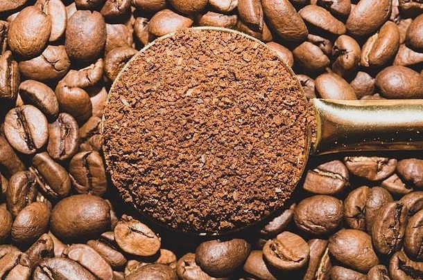 一勺磨碎的咖啡放在烤咖啡豆里