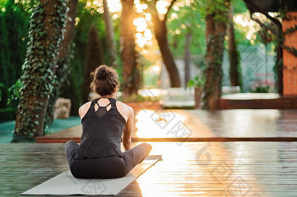 在热带岛屿的木甲板上，一位有着东方容貌的年轻女子独自练习瑜伽。运动、健身、健康的生活方式理念。