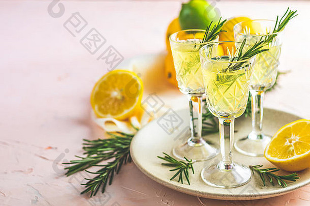 传统意大利柠檬酒精饮料limoncello利口酒，淡粉色、桃红色或珊瑚色的石头上有柠檬和迷迭香药草片