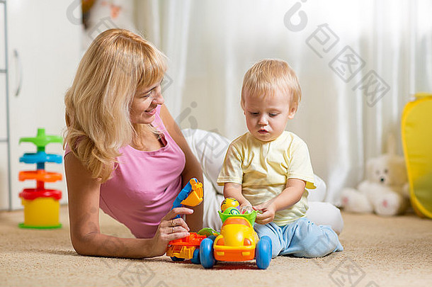 妈妈。蹒跚学步的儿子玩玩具车托儿所地板上